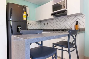 Una cocina compacta equipada con refrigerador, microondas y estufa a gas.