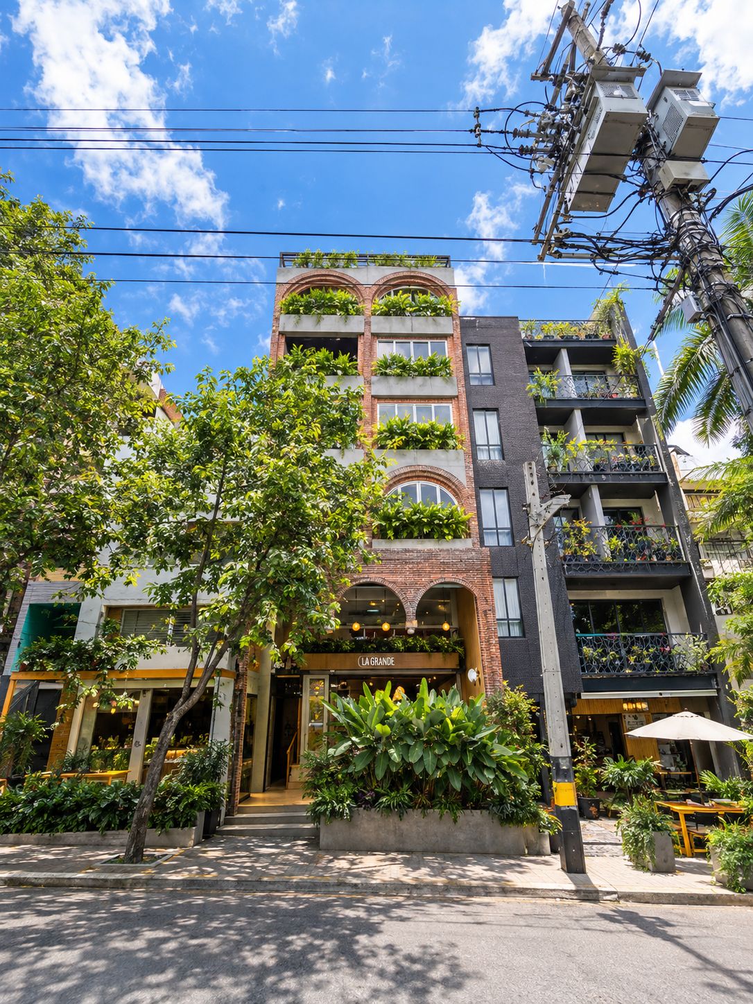 A multi-story building with balconies, a ground-level entrance, and a visible restaurant with outdoor seating.