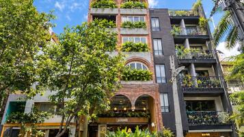 A multi-story building with balconies, a ground-level entrance, and a visible restaurant with outdoor seating.