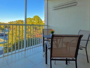Un balcon avec une table et des chaises, un pot de fleurs et une vue sur des arbres et un parking.