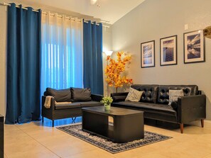Una sala de estar con un sofá seccional, una mesa de centro y un ventanal con cortinas azules.