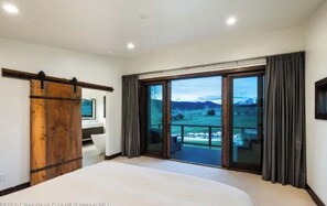 Ein Schlafzimmer mit einem großen Bett, einer Schiebetür zu einem Balkon und Blick auf eine Berglandschaft.