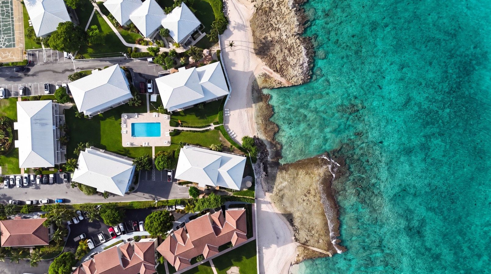 Vue aérienne d’un hôtel situé sur la côte, composé de plusieurs bâtiments, avec une piscine et une plage.