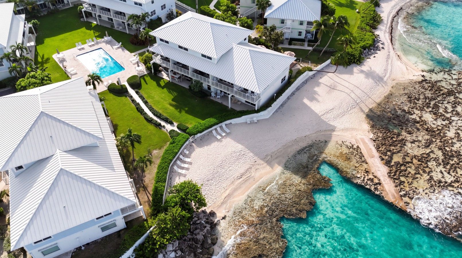 Un complexe hôtelier comprenant plusieurs bâtiments, une piscine et une plage bordée d’une eau turquoise et cristalline.