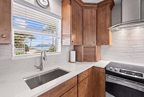 A kitchen with a stainless steel sink, wooden cabinets, a built-in oven, and a window with blinds. - New Re-Furnished 2bd Condo with Ocean Views from Every Room on Seven Mile Beach (George Town)