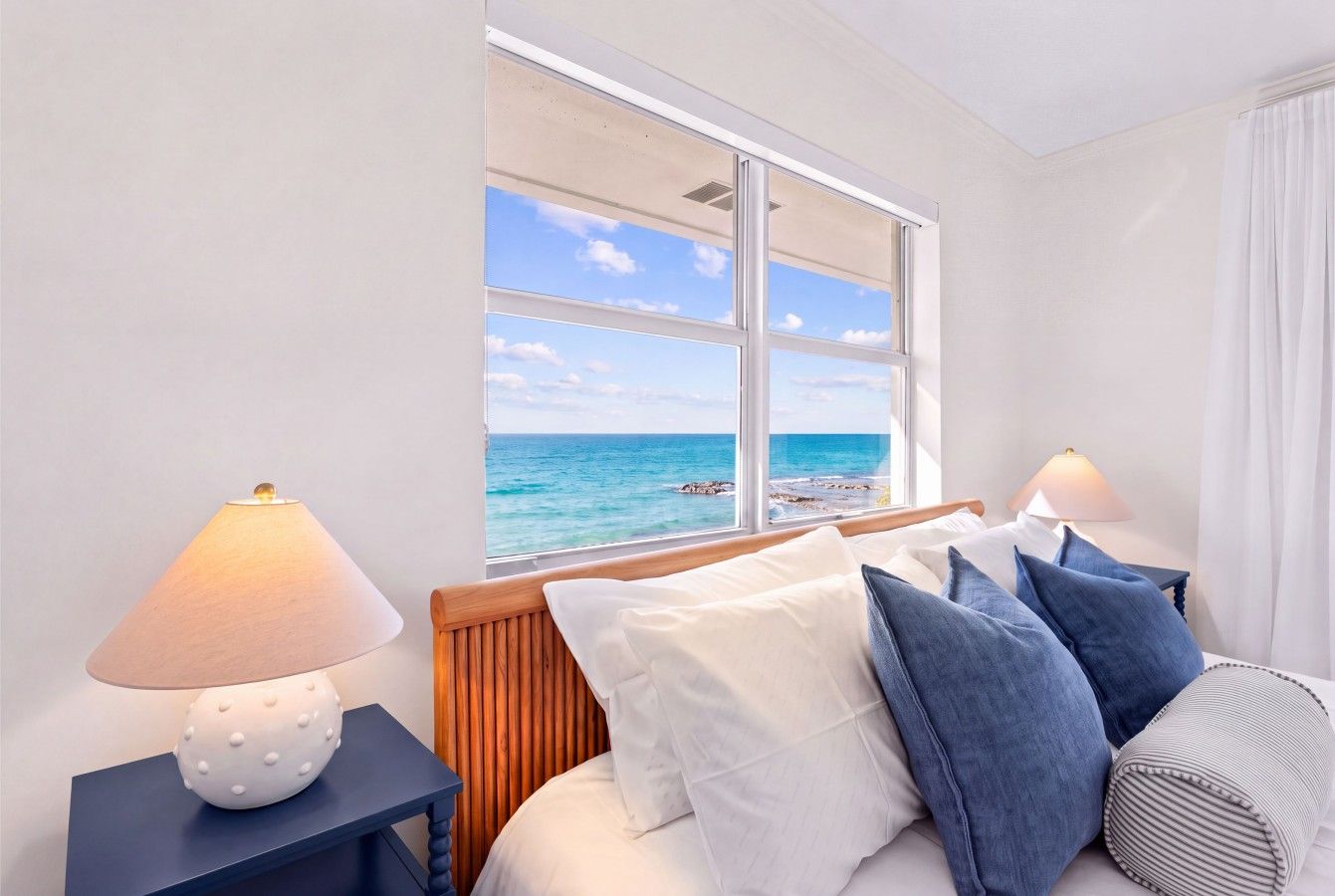 Une chambre d’hôtel avec un lit, deux tables de chevet, une lampe et une fenêtre donnant sur la mer.
