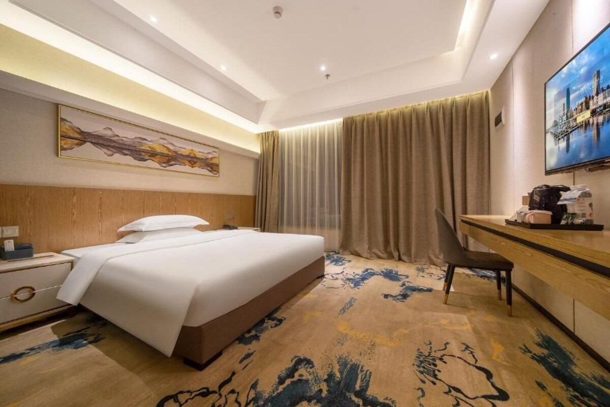 Ein Hotelzimmer mit Bett, Schreibtisch, Stuhl, Fernseher und einem Bild an der Wand.