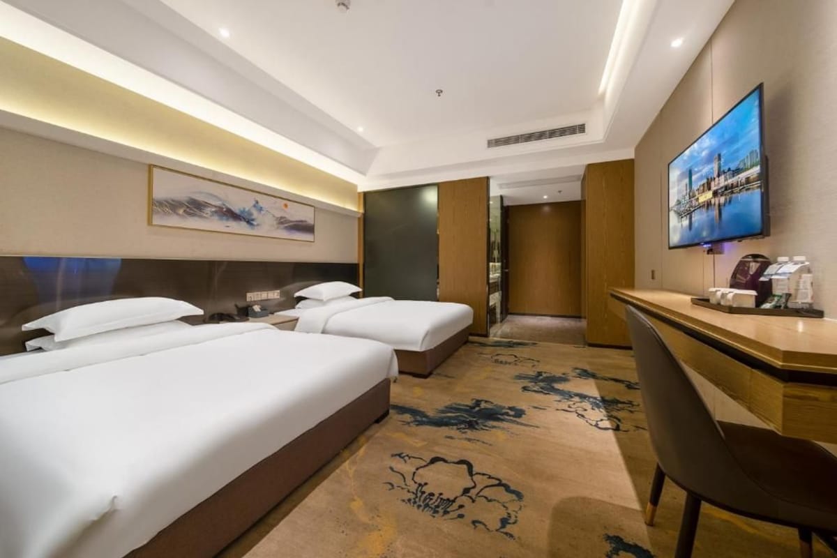 Ein Hotelzimmer mit zwei Betten, einem Schreibtisch, einem Fernseher und einem großen Fenster.