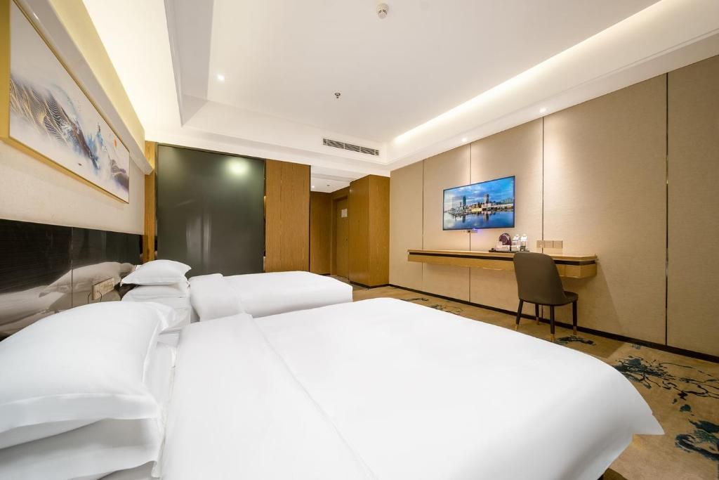 Una habitación de hotel con dos camas, un escritorio, una silla y un televisor en la pared.