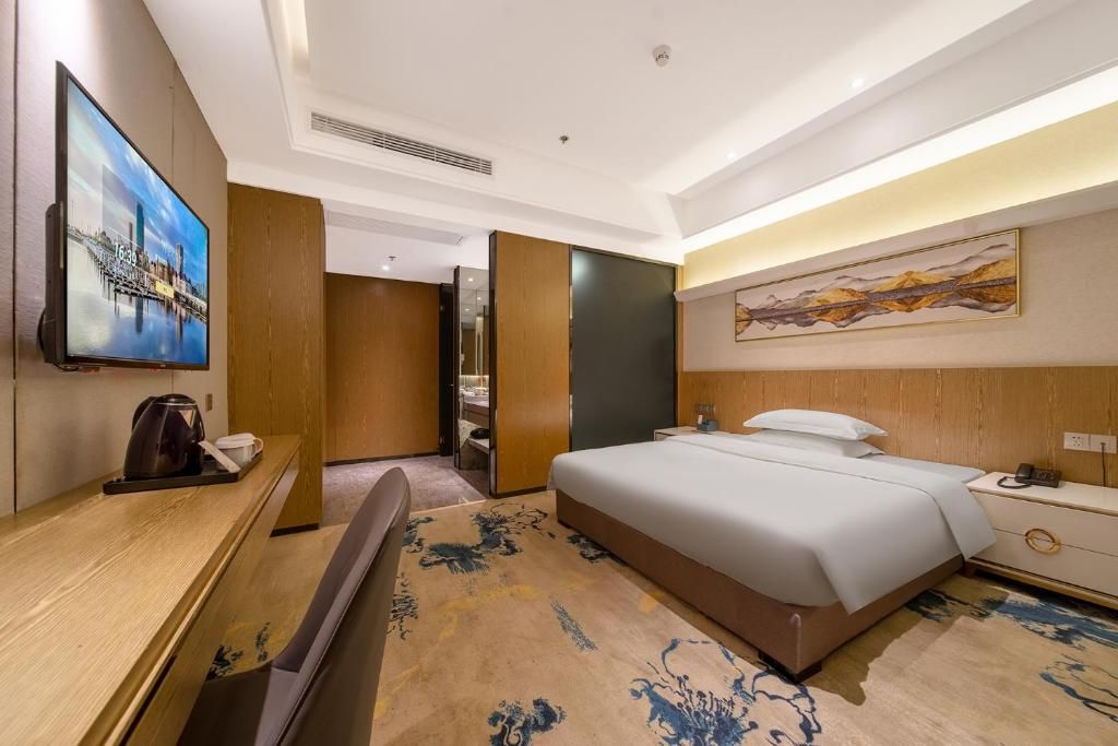 A hotel room with a bed, bedside table, TV, and a painting on the wall.
