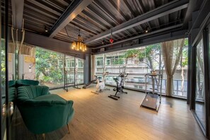 Ein modernes Fitnessstudio mit Trainingsgeräten, großen Fenstern und einem grünen Sofa.