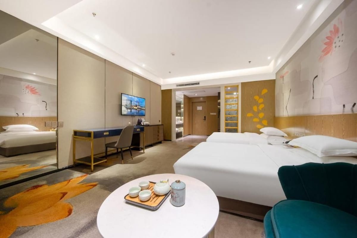 Ein Hotelzimmer mit Bett, Schreibtisch, Stuhl und rundem Tisch mit Tablett.