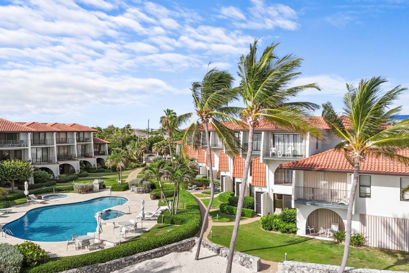 Un resort con piscina, palmeras y edificios de varios pisos con techos de tejas rojas.