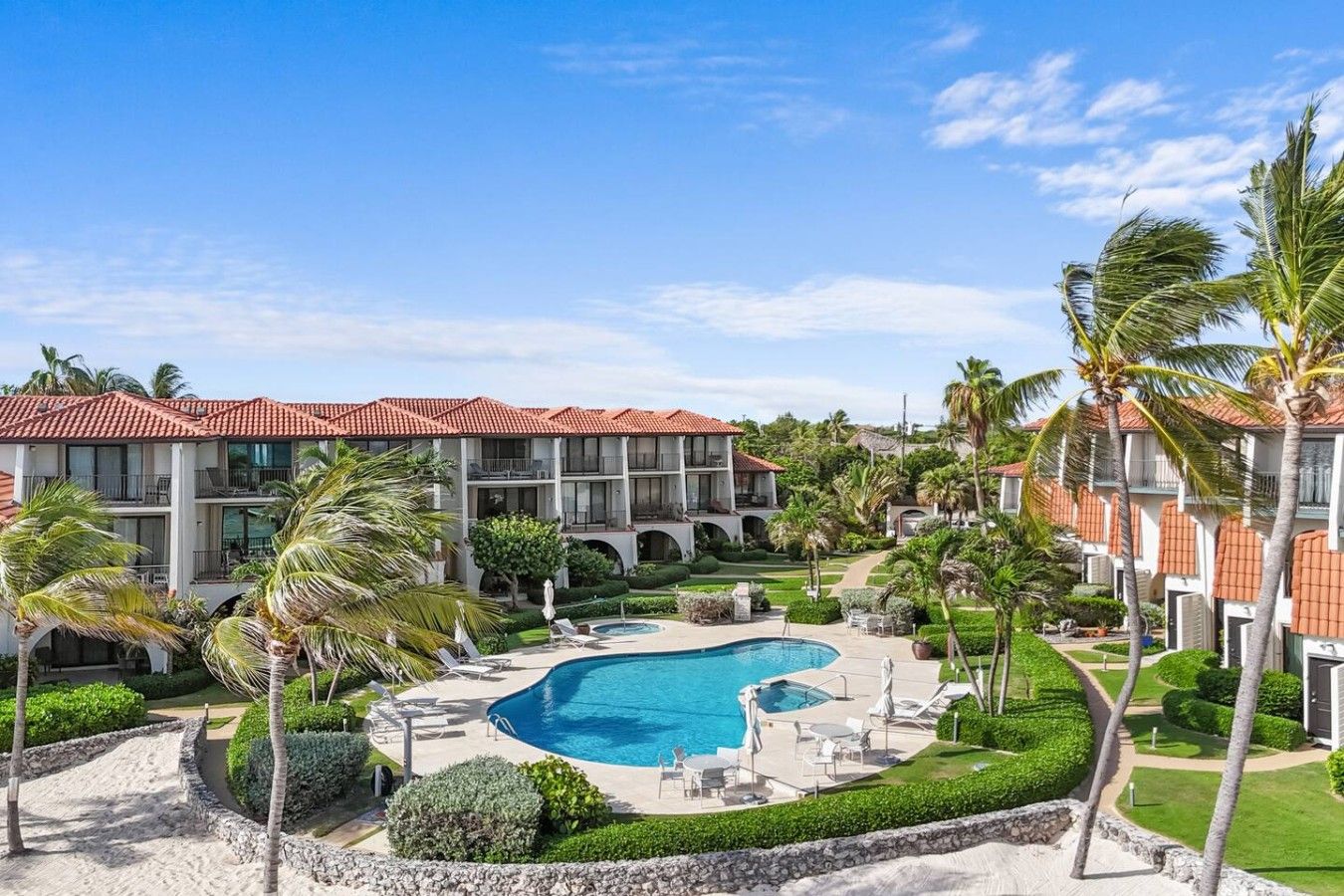 Un resort con piscina, palmeras y un edificio con techo de tejas rojas.