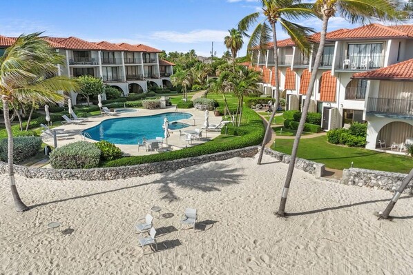 A resort with a swimming pool, lounge chairs, and palm trees.