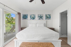 A bedroom with a large bed, a balcony with a chair, and a door leading to a bathroom. - Newly Renovated Beachfront 2BR w Ocean & Pool View (George Town)