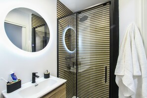 A modern bathroom with a round mirror, a white sink, and a glass-enclosed shower. - Terrific 3-bedroom apartment in the heart of Pamplona (Pamplona)