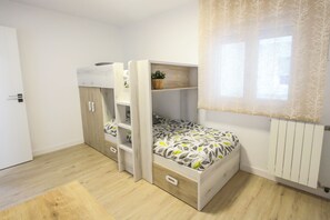 Una habitación con literas, un escritorio pequeño, un radiador y una ventana con cortinas.