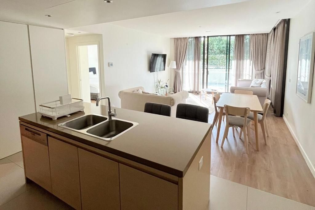 A modern kitchen with a central island, a dining area with a table and chairs, and a living space with a sofa and a TV.