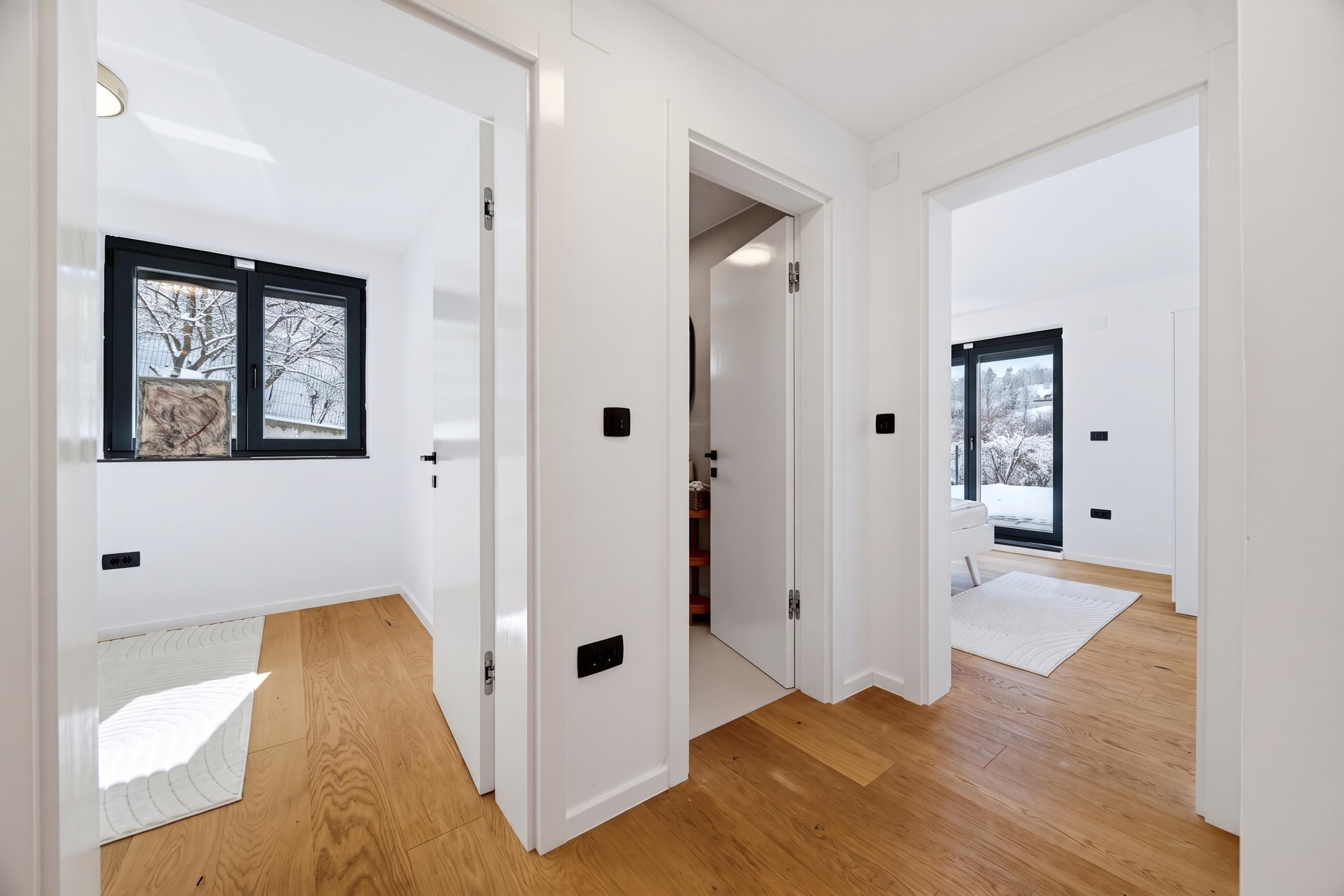 A modern interior with white walls, wooden flooring, and a view of a snowy landscape through a window.