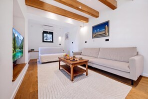 A modern living room with a white sofa, a wooden coffee table with fruits and pastries, and a painting on the wall. - Green Zone Apartment With Terrace And Parking, Zagreb, Croatia (Zagreb)
