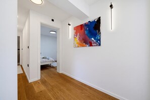 A hallway with wooden flooring, a bed with a white headboard, and a colorful abstract painting on the wall. - Green Zone Apartment With Terrace And Parking, Zagreb, Croatia (Zagreb)