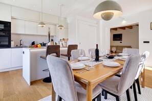 A modern kitchen with white cabinets, a dining area with a wooden table set for six, and a large pendant light above the table. - Green Zone Apartment With Terrace And Parking, Zagreb, Croatia (Zagreb)