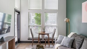 Ein modernes Wohnzimmer mit Fernseher, einer Couch, einem Couchtisch und einem Essbereich mit Stühlen und einer Pflanze.