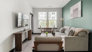 A modern living room with a flat-screen TV, a dining table with chairs, a sofa, and a coffee table. - Landing | Stylish 1BD (Nashville)