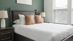 A neatly made bed with white bedding and two brown pillows, a dark wooden headboard, and bedside lamps on a nightstand. - Landing | Chic 1BD - One Bedroom Apartment, Sleeps 2 (Nashville)