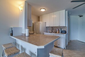A modern kitchen with white cabinets, a central island, and a built-in microwave. - Oceanfront Kihei Condo | Ground Floor, Pool, Hot Tub & AC (Kihei)