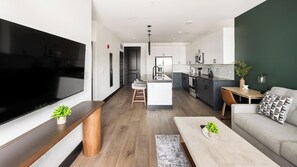 A modern apartment with a large TV, a kitchen with a central island, and a seating area with a sofa and coffee table. - Landing | Modern 1BD (Nashville)