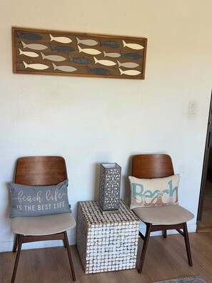 Two wooden chairs with matching cushions, a decorative fish wall art, and a patterned box between them. - Tropical Garden Retreat at Oceanfront Paki Maui (Lahaina)