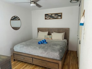 A bedroom with a bed, a ceiling fan, a wall-mounted mirror, and a framed picture. - Tropical Garden Retreat at Oceanfront Paki Maui (Lahaina)