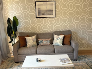 A living room with a grey sofa, a white coffee table, and a framed picture on the wall. - Tropical Garden Retreat at Oceanfront Paki Maui (Lahaina)