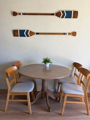 A round wooden table with four chairs, a small potted plant, and two decorative wooden paddles on the wall. - Tropical Garden Retreat at Oceanfront Paki Maui (Lahaina)