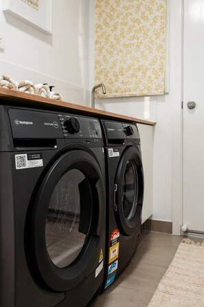 A front view of a washing machine and dryer in a laundry room with a wooden countertop above. - Salt Bush | Swim Spa | Close to Everything (Bicheno)