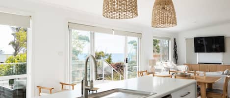 Una cocina moderna con una isla grande, pileta de acero inoxidable y lámparas colgantes de mimbre.
