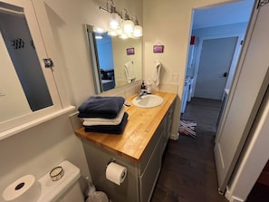 Ein Badezimmer mit einem Holzkosmetikschrank, einem Waschbecken, einer Toilette und einem beleuchteten Spiegel.