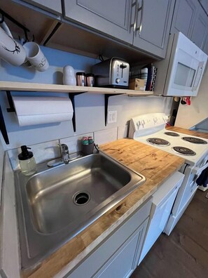 Een keuken met een roestvrijstalen spoelbak, een houten aanrecht, witte kastjes en een witte kookplaat.