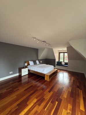 Ein Schlafzimmer mit einem hölzernen Bett, einem Nachttisch, einer Bank und einem Fenster mit Jalousien.