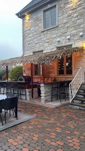 A stone building with a brick patio, outdoor seating, and a barbecue area. - Luxury Estate Home | Cinema & Sauna (Candiac)