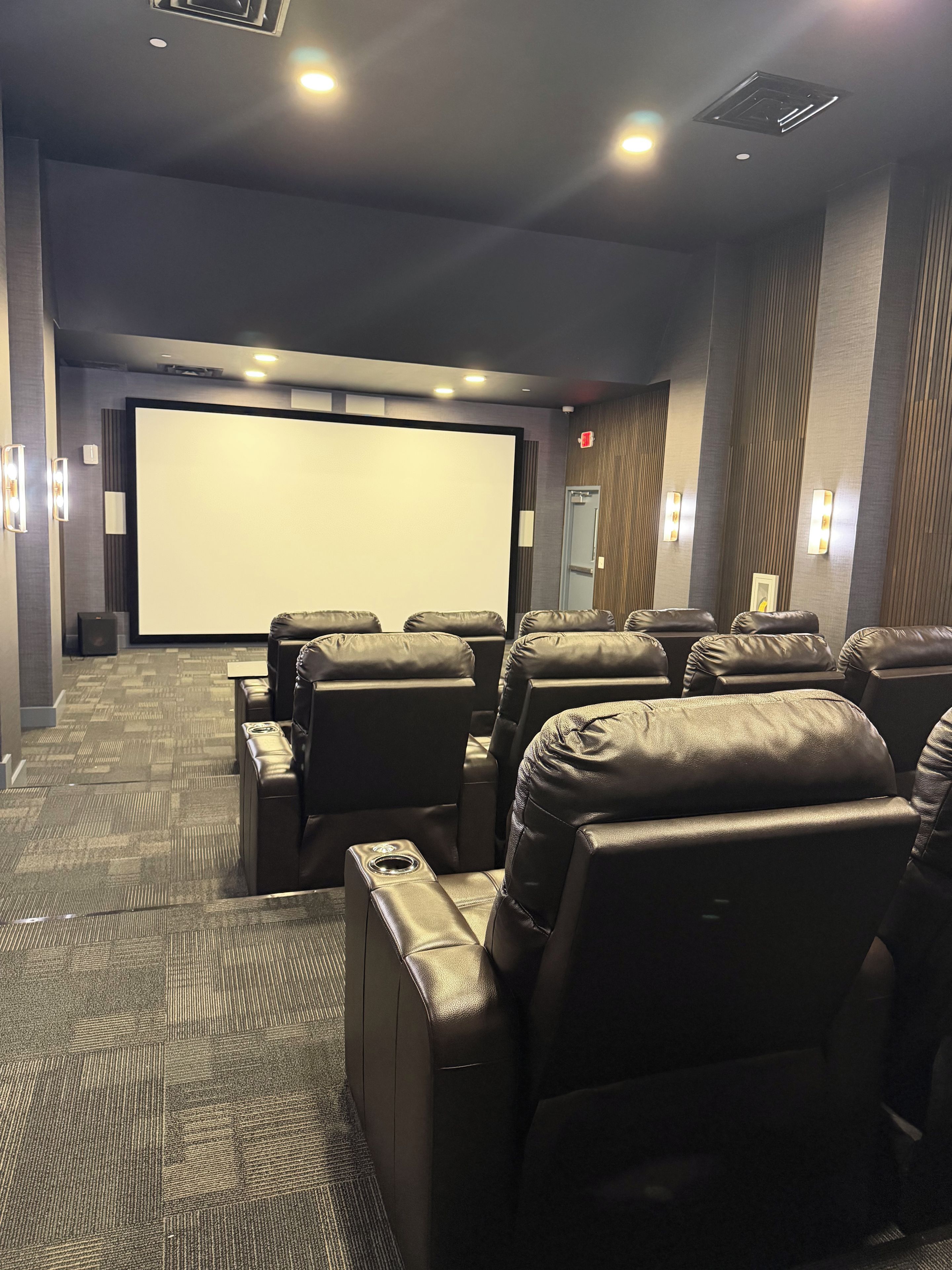 Une salle de cinéma dotée de rangées de fauteuils inclinables en cuir, d’un grand écran et de haut-parleurs fixés aux murs.