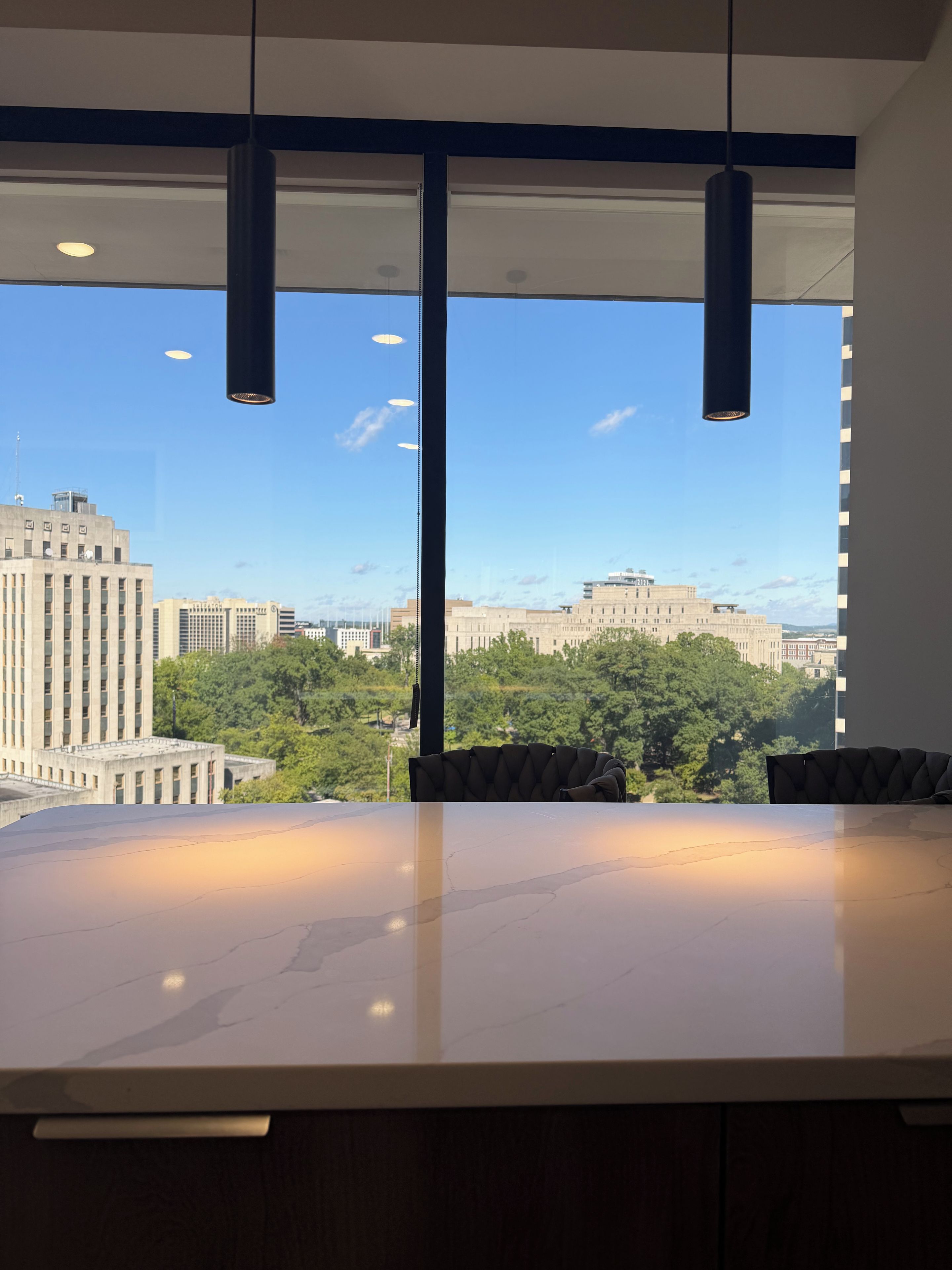 A modern interior with a large table and chairs, large windows with a cityscape view, and pendant lighting.
