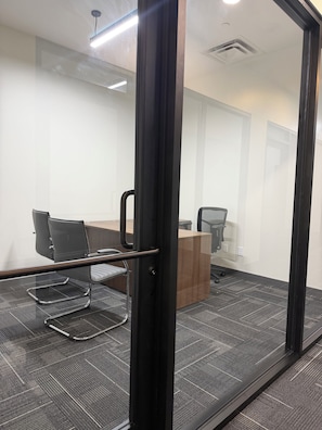 A conference room with a glass partition, a wooden desk, two chairs, and a carpeted floor. - Modern Condo In Downtown Birmingham Near UAB (Birmingham)