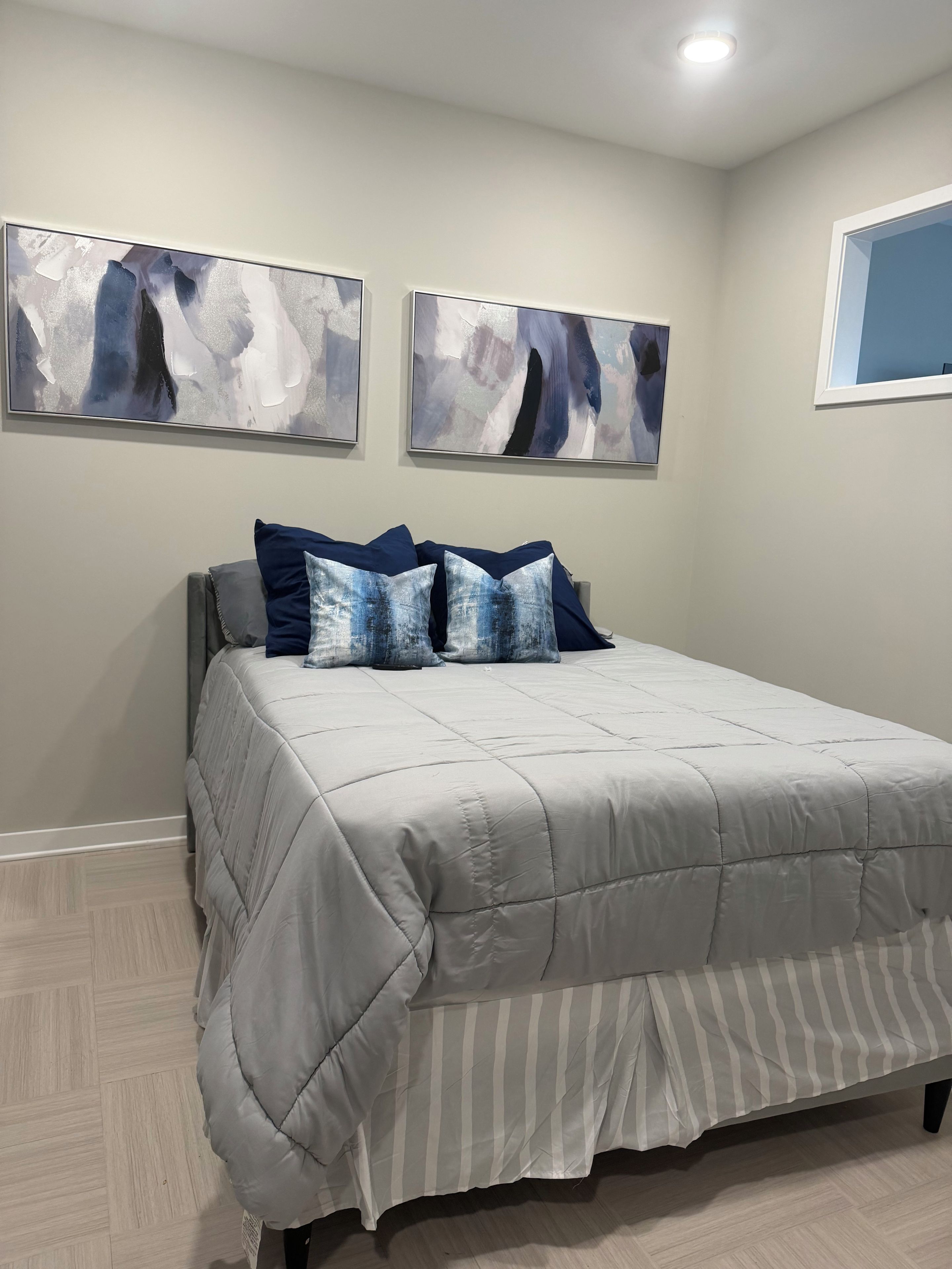Une chambre à coucher avec un lit, deux tableaux abstraits et une fenêtre.