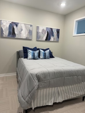 Une chambre à coucher avec un lit, deux tableaux abstraits et une fenêtre.
