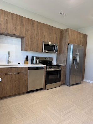 Une cuisine moderne avec des meubles en bois, des appareils en acier inoxydable, un lave-vaisselle et un plancher à motifs en chevrons.