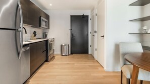 A modern kitchen with stainless steel appliances, a wooden floor, and a dining area with a table and chairs. - Landing | Chic 1BD, Pool, Courtyard (Orlando)