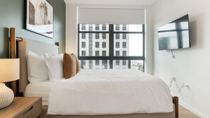 Quarto de hotel com uma cama grande, televisão fixada na parede e janela com vista para edifícios.